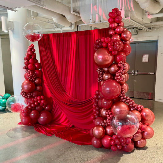 Decorative balloon arch with red and chrome red balloons in front of a red curtain.