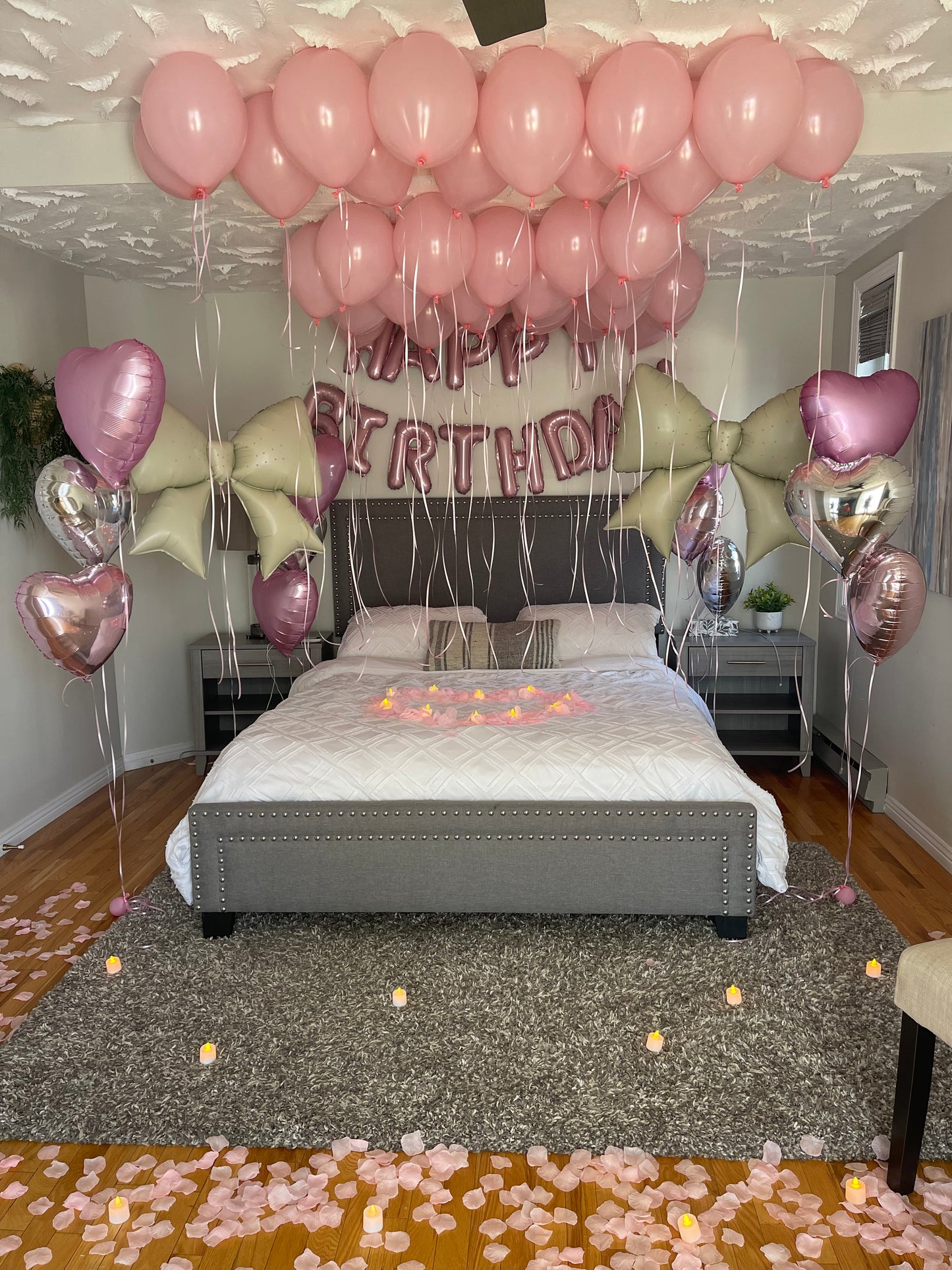 Decorative setup with pink latex balloons, foil bows, and 'Happy Birthday' script balloon on a wall