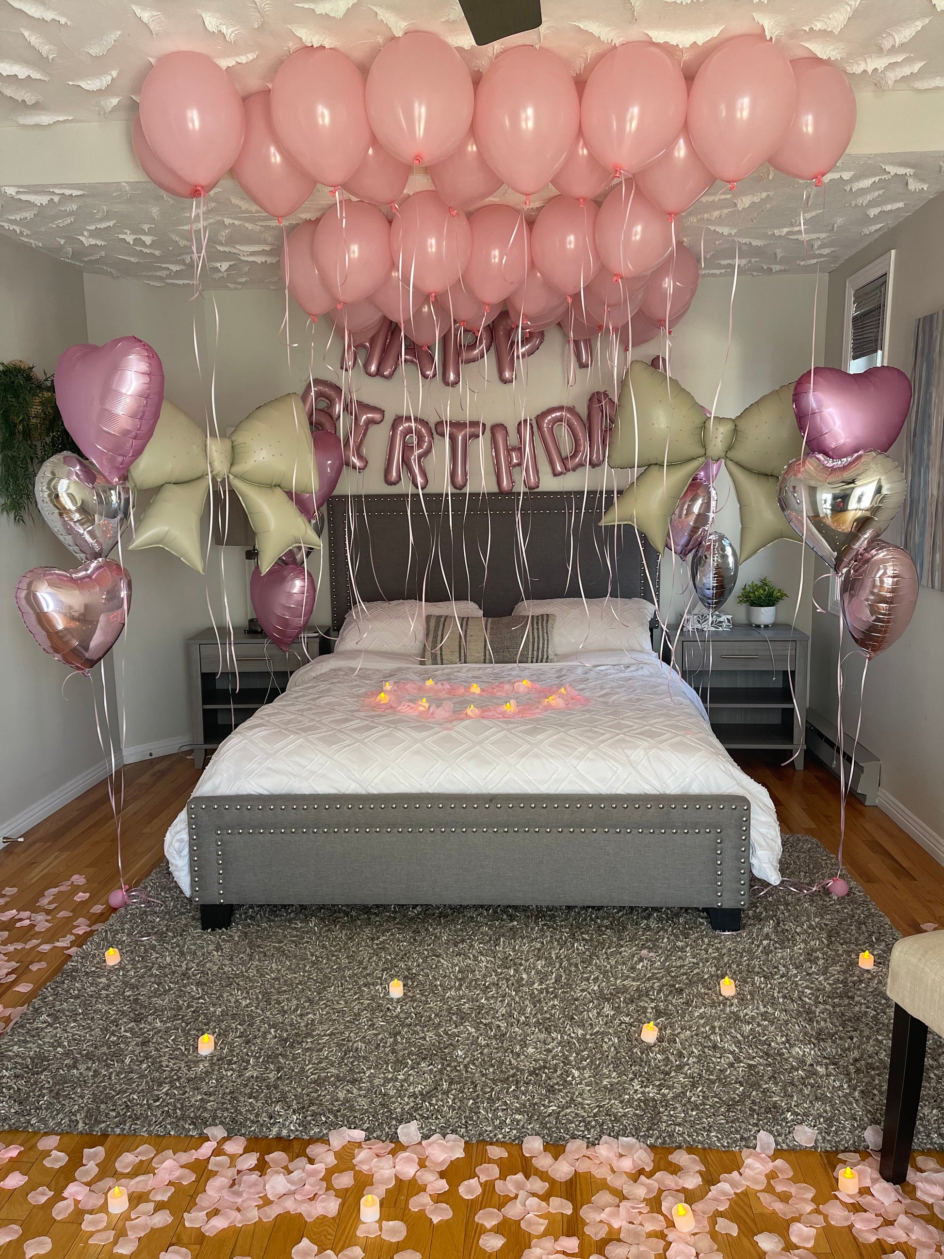 Decorative setup with pink latex balloons, foil bows, and 'Happy Birthday' script balloon on a wall