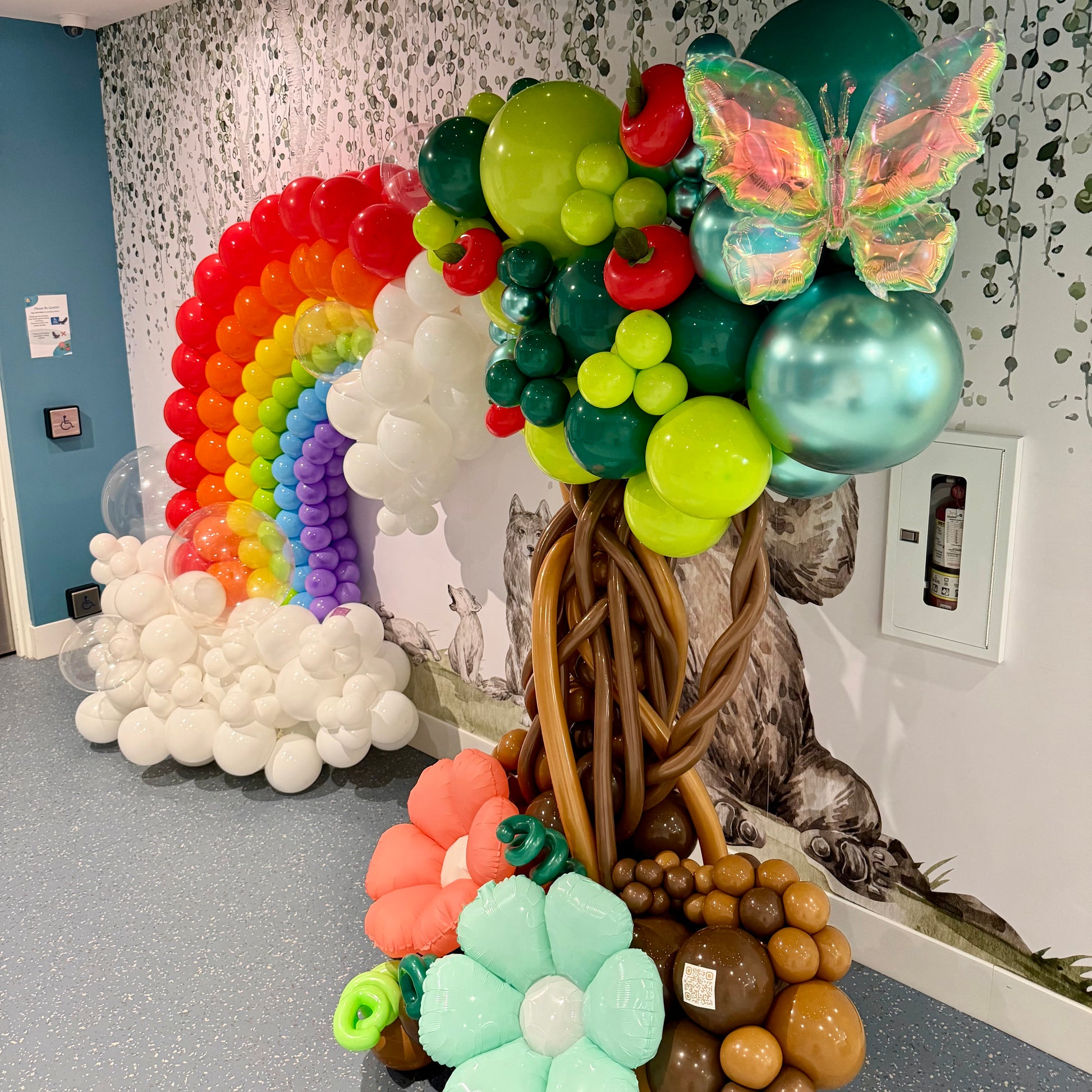 Colorful balloon decorations including a rainbow, tree, and butterfly in an indoor setting.