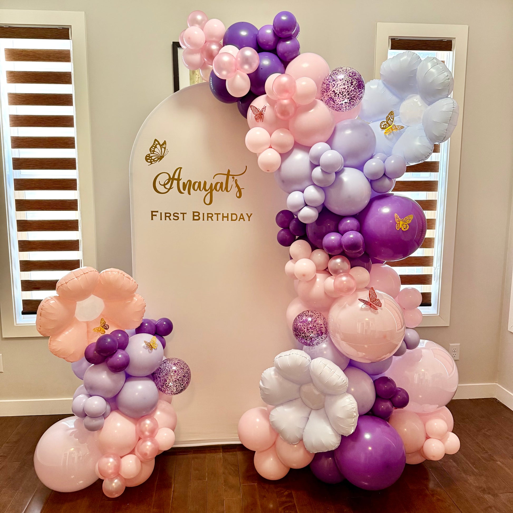Balloon arch for a first birthday party with custom vinyl text on a beige backdrop.