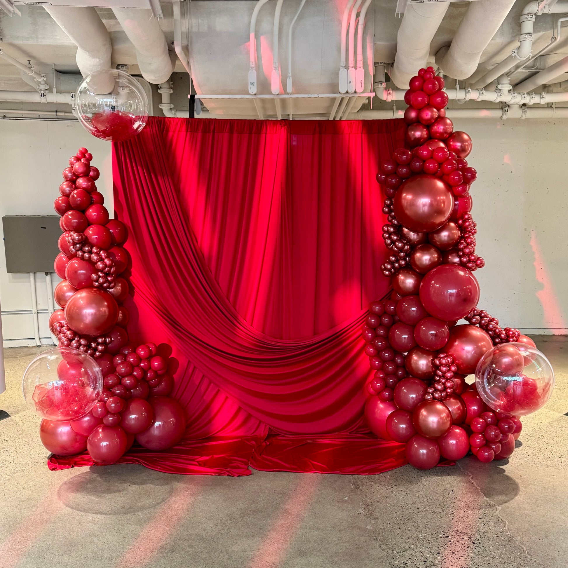 Red balloon arch with a red curtain in an indoor setting
