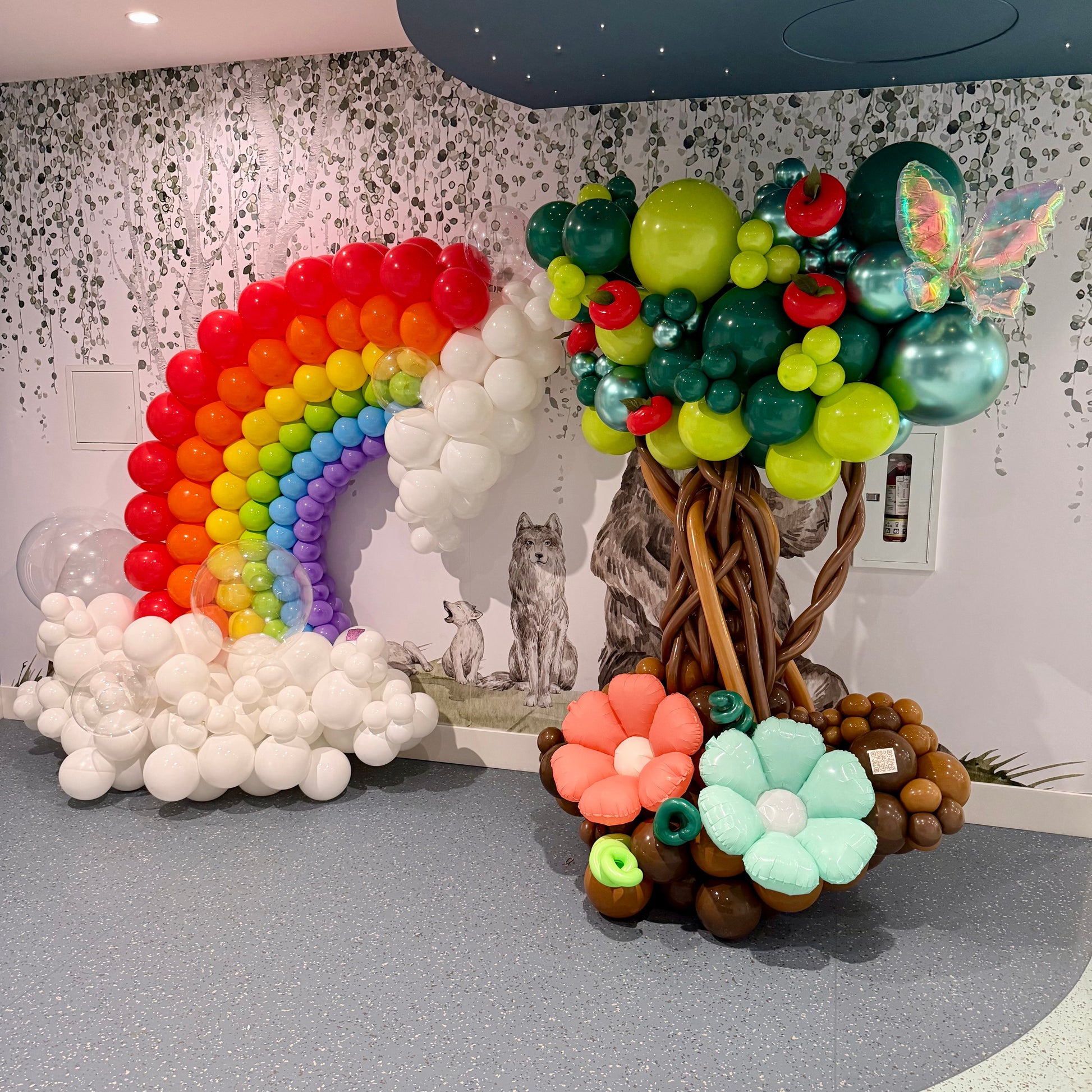 Balloon decorations including a rainbow, tree, and flowers in a room setting.