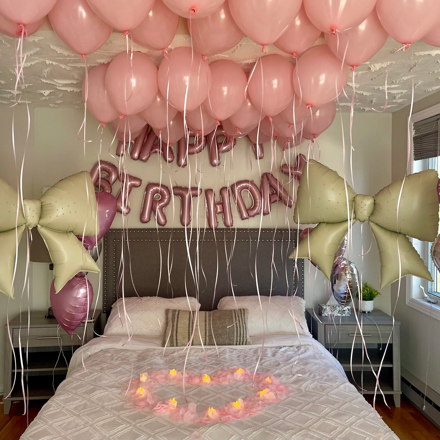 Bedroom decorated with pink balloons, 'Happy Birthday' banner, and candles on a bed.