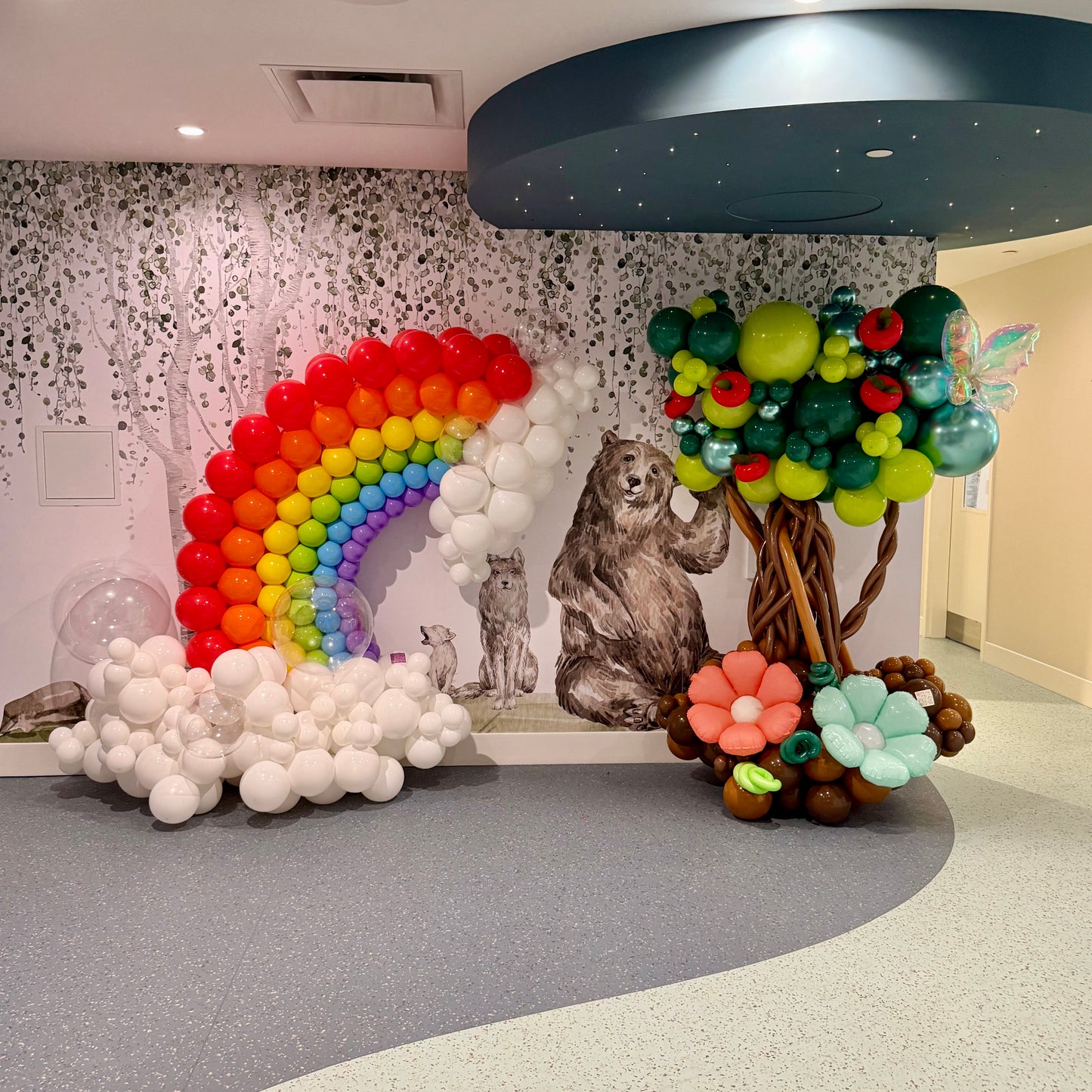 Colorful balloon decorations including a rainbow, bear, and tree in a room setting.