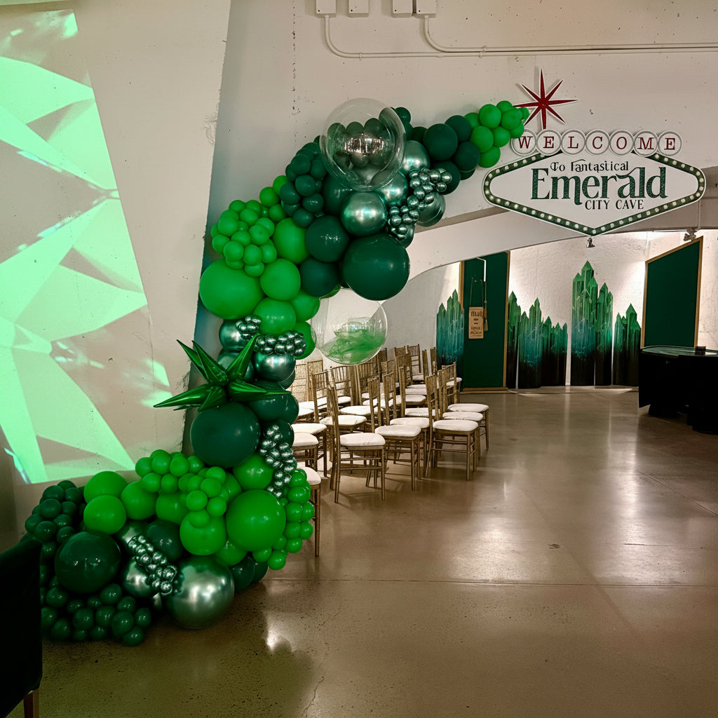 Green balloon archway with chairs and 'Welcome to the Fantastical Emerald City Cave' sign.