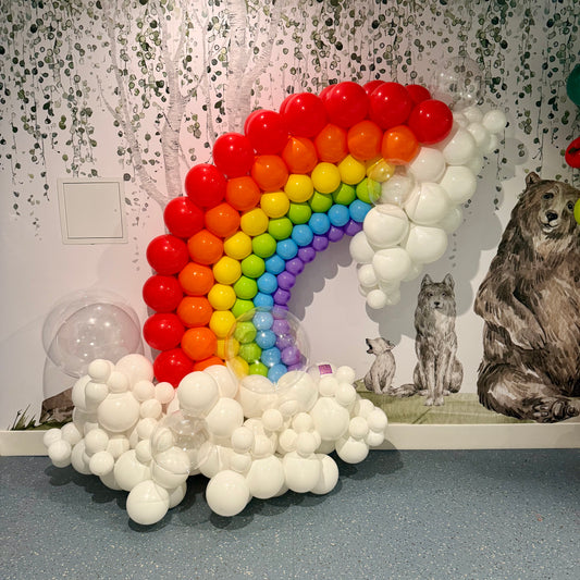 Balloon arch shaped like a rainbow with white balloons, featuring animals on a wall.
